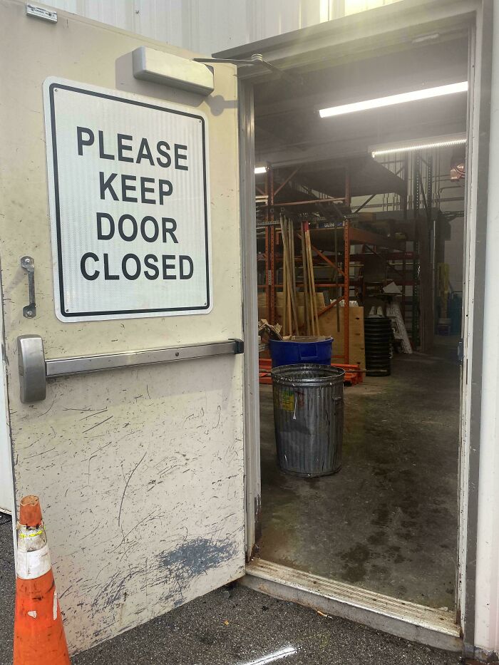 Industrial door with a please keep door closed sign open to a warehouse, symbolizing first-world anarchists defying rules.