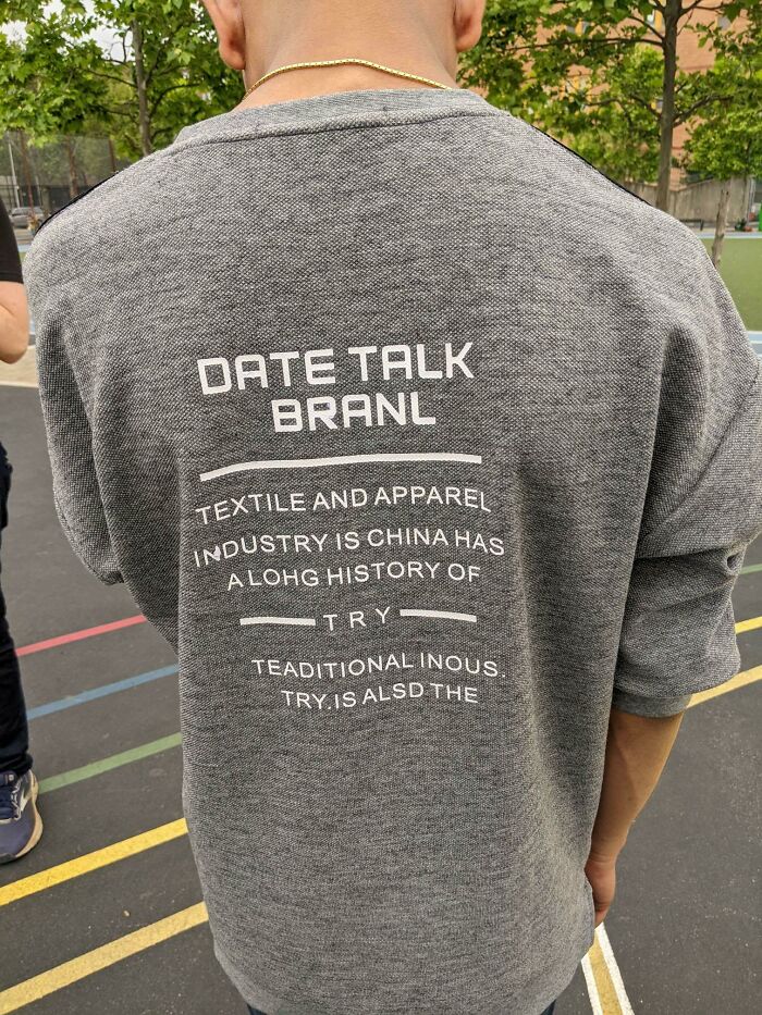 Gray t-shirt with hilariously bad text print containing misspellings and confusing phrases outdoors.