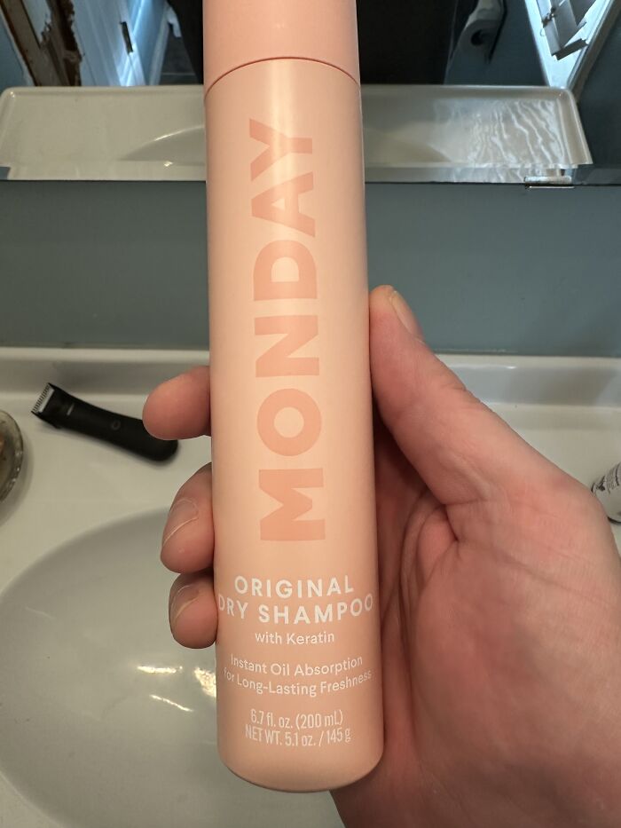 Hand holding a bottle of Monday original dry shampoo with keratin for instant oil absorption and long-lasting freshness.