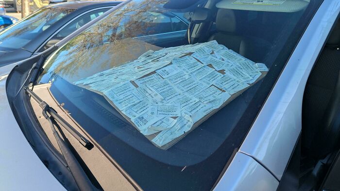 Car windshield covered with numerous parking tickets, illustrating first-world anarchists defying rules and authority.
