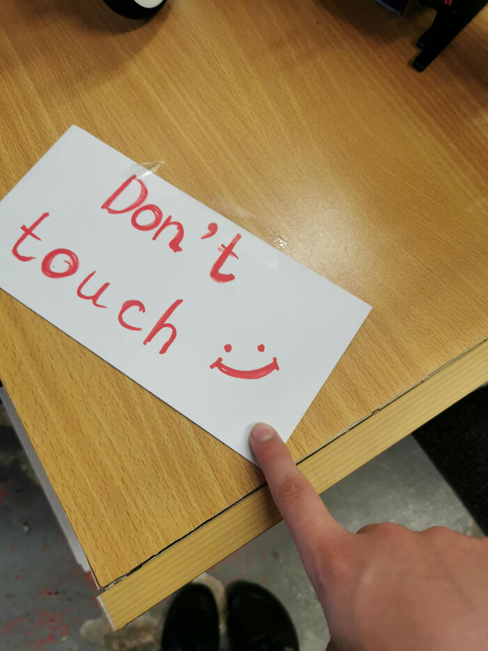 Hand pointing at a handwritten "Don't touch" sign on a wooden table reflecting first-world anarchists' ungovernable mindset.