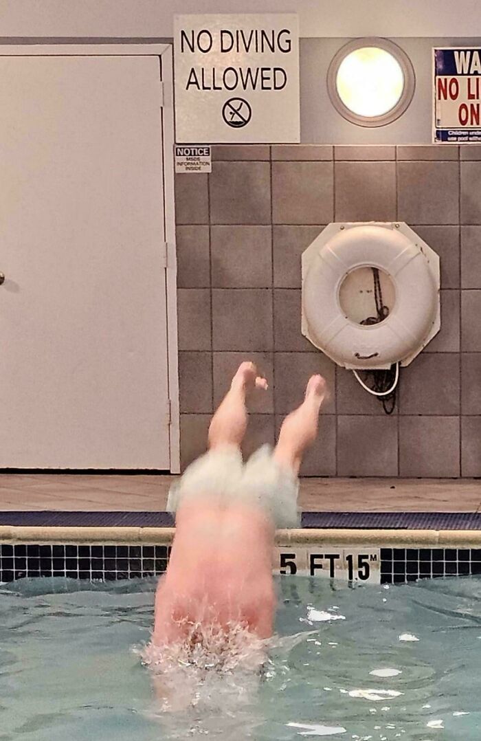 Person defiantly diving into pool beneath no diving allowed sign, embodying first-world anarchist rebelliousness.