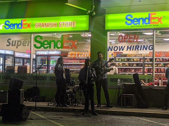 Band performing outside a store named SendEx, a hilariously shameless copy of famous brand FedEx at night.