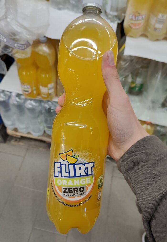 Bottle of orange soda labeled Flirt zero, a shameless copy of famous brand packaging, held in a store aisle.