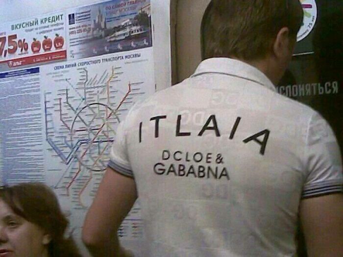 Man wearing a hilariously bad T-shirt design with misspelled brand and country name on the back in a public space.