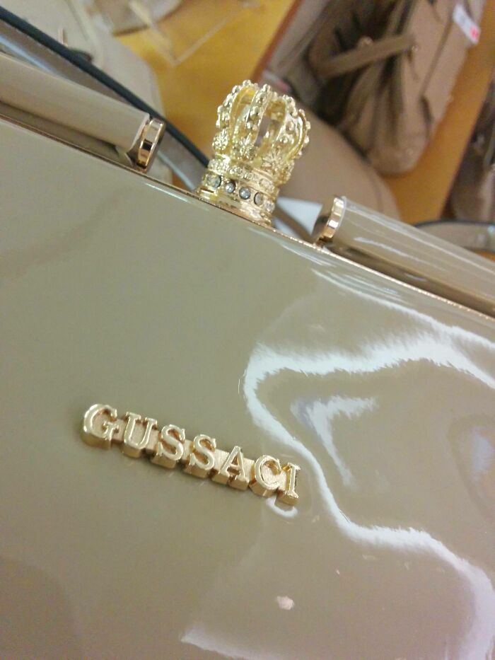 Close-up of a handbag with a crown detail and a shamelessly copied brand name resembling Gucci in design.