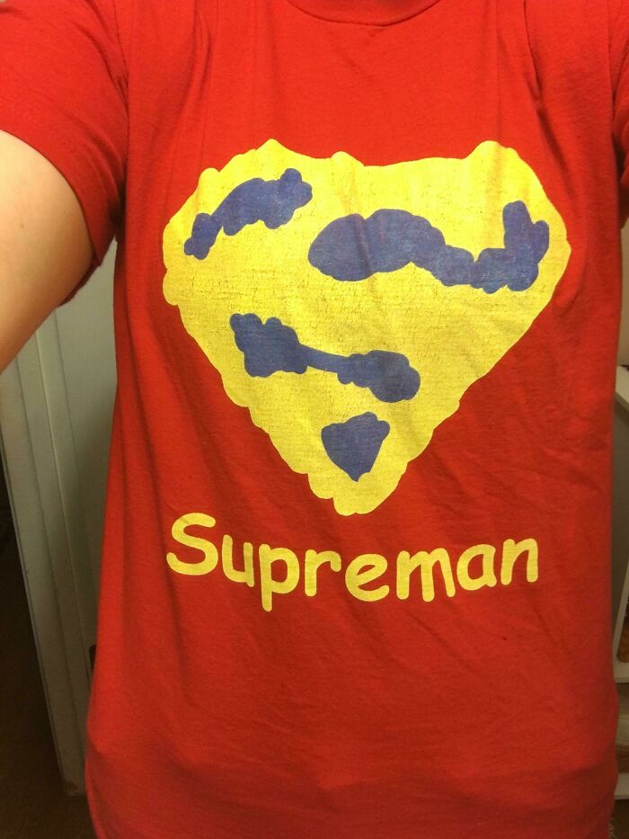 Red t-shirt with a poorly designed yellow and blue superhero emblem and the misspelled word Supreman.
