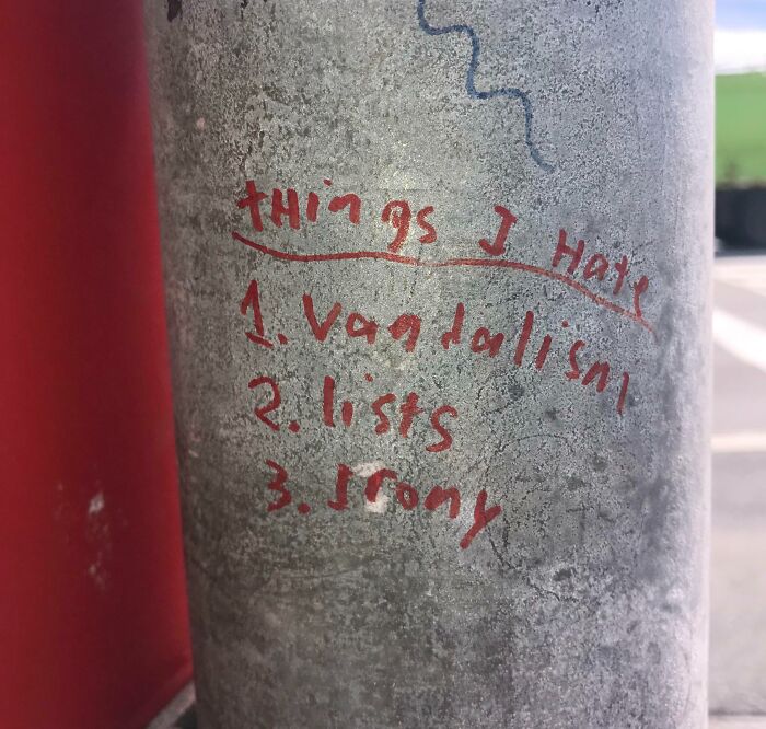 Red graffiti listing "things I hate" including vandalism, on a weathered metal pole, an example of mild vandalism.