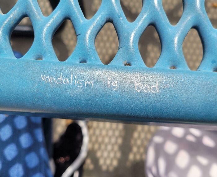 Blue metal bench with faint white chalk writing vandalism is bad, showing mild vandalism in a public setting.