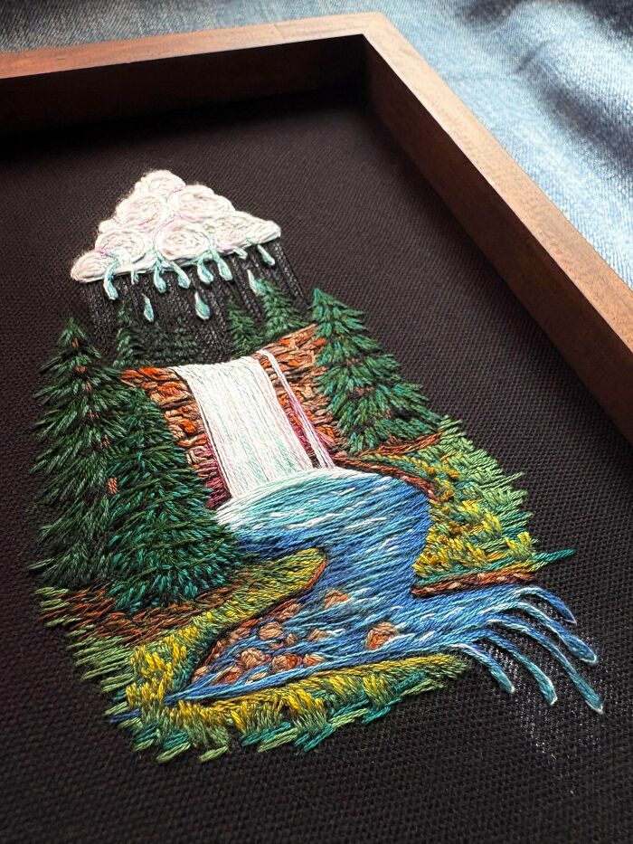 Detailed embroidery creation of a waterfall scene with trees and a cloud, inspiring hobby.