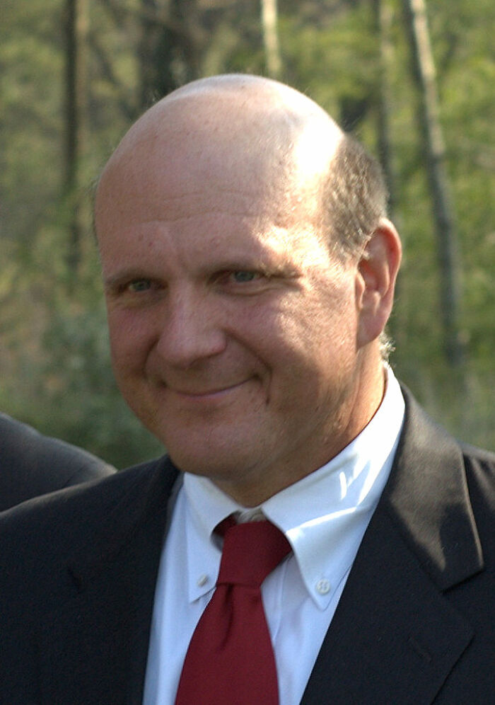 Steve Ballmer smiling outdoors, wearing a suit and red tie, representing key bio and career highlights.