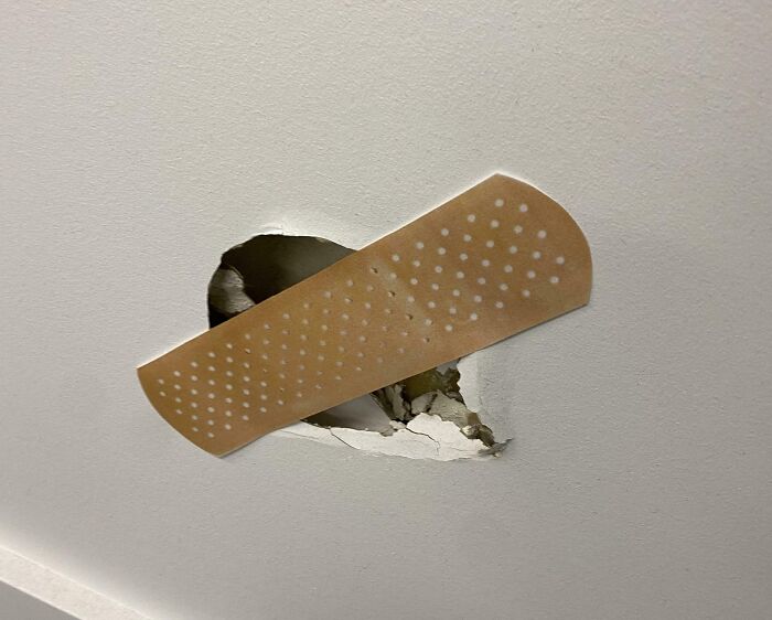 Wall hole patched with an adhesive bandage, symbolizing makeshift workplace repairs and frustration at work.