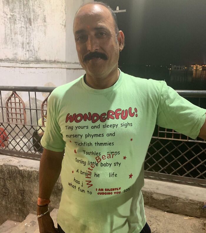 Man wearing a hilariously bad T-shirt with misspelled words and confusing text design at night outdoors.