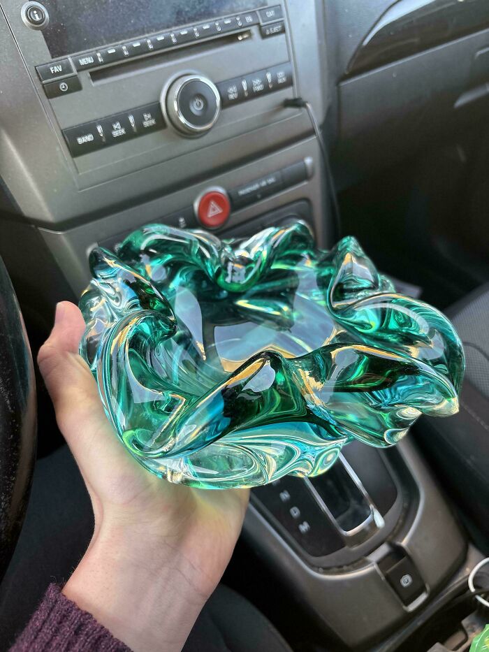 Hand holding a creative and cool teal glass item with wavy edges inside a car interior.