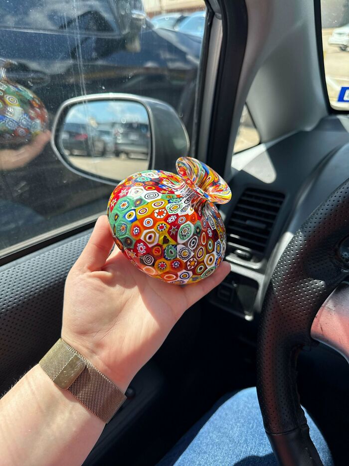 Hand holding a colorful, creative glass paperweight with intricate patterns inside a car, showcasing unique glass items.