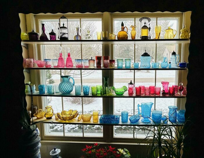 Colorful and creative glass items displayed on shelves in front of a window, perfect unique glass décor for your home.