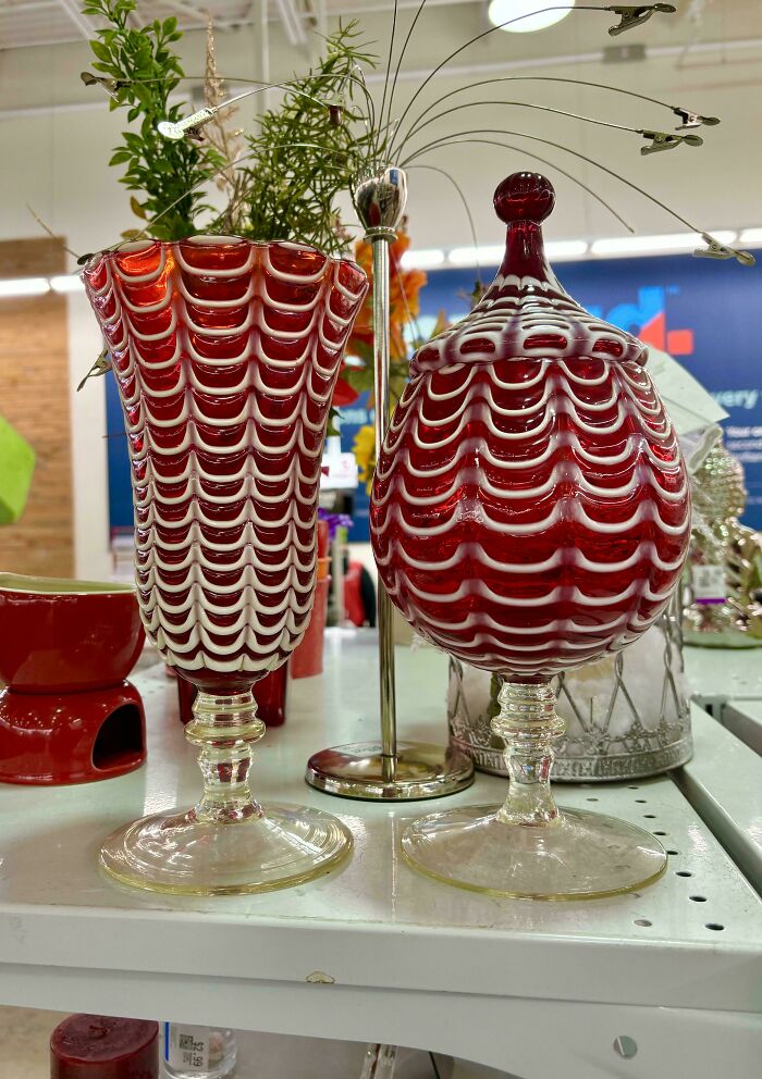Red and white patterned decorative glassware displayed on a shelf among other creative glass items.