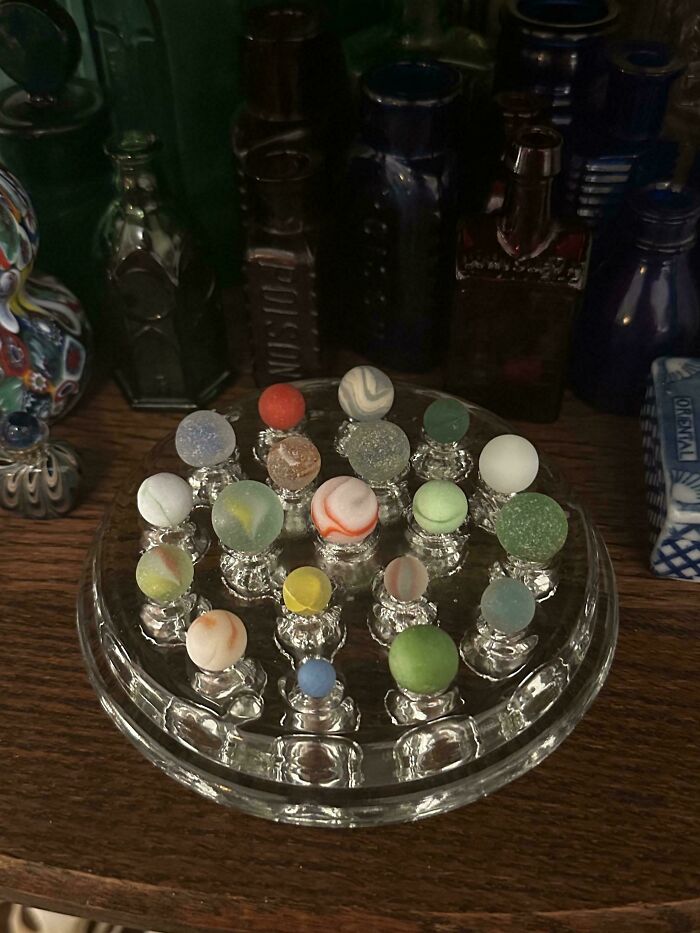 Colorful glass marbles displayed on a clear glass stand among various creative glass items for the home.