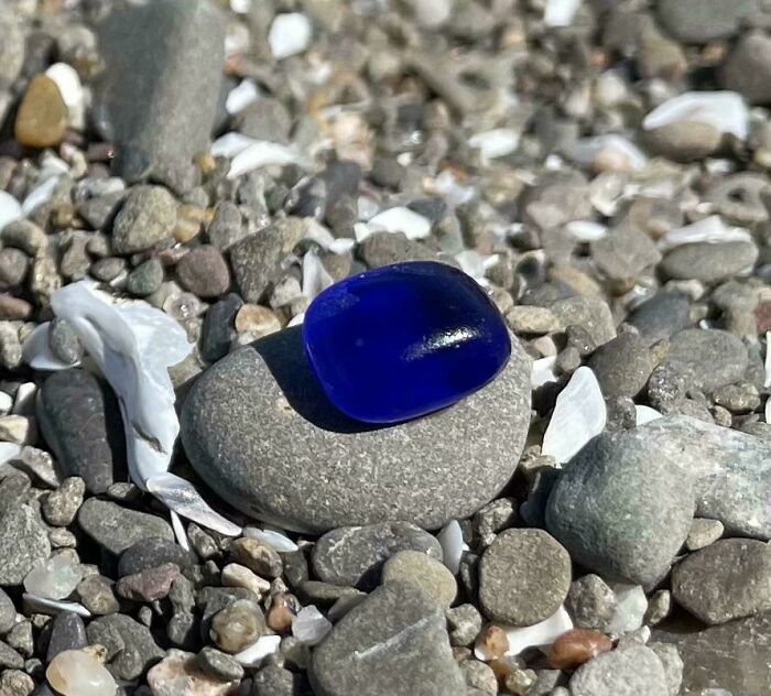 Smooth blue glass item resting on gray pebbles among other stones, showcasing cool and creative glass items.