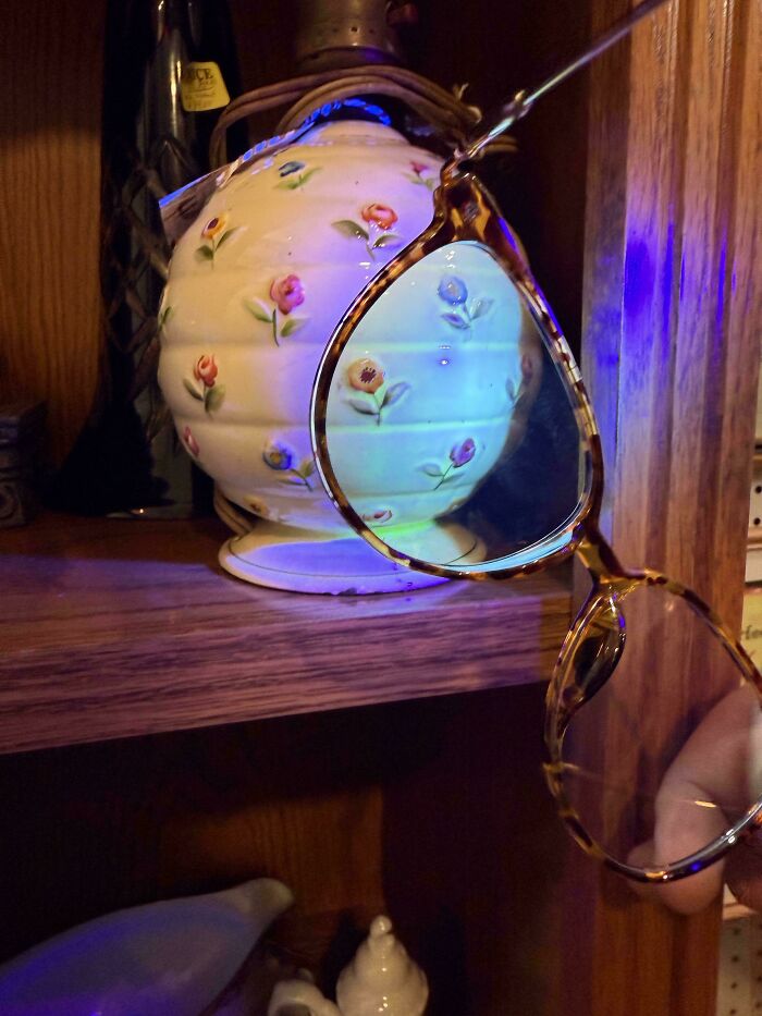 Tortoiseshell framed eyeglasses held up showing floral glass vase through the lens on a wooden shelf.