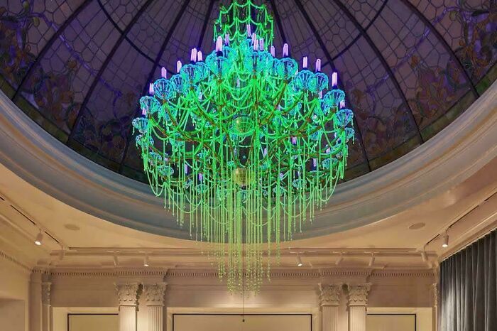 Large creative glass chandelier with green and purple lights hanging in an elegant room under a dome ceiling.