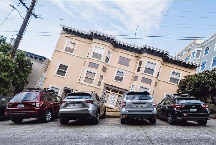 Tilted house on a steep street with parked cars, an unedited photo that might mess with your tired brain.