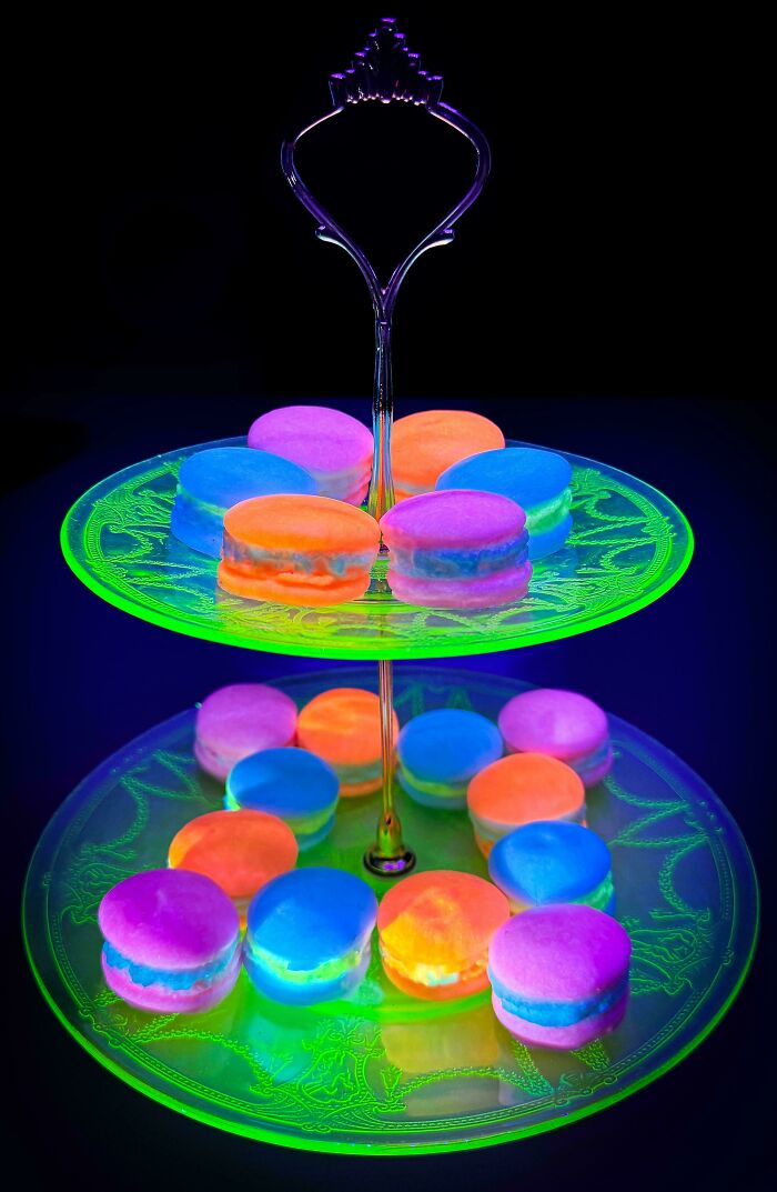 Two-tiered creative glass serving stand holding colorful glowing macarons under blacklight.