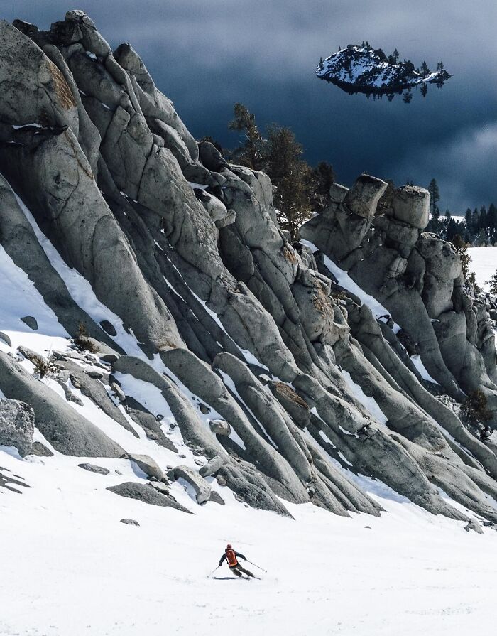 Skier descending snow-covered mountainside with rocky formations and an oddly shaped floating snow island in the sky, brain-messing photo.