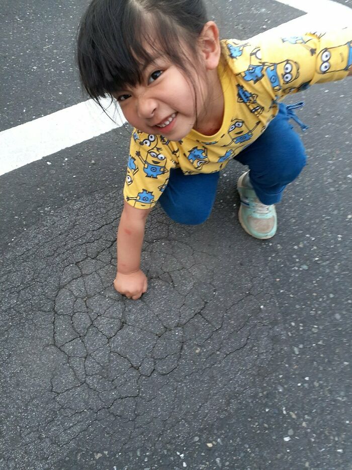 Young girl in creative pose crouching on cracked pavement wearing a yellow Minions shirt and blue pants.