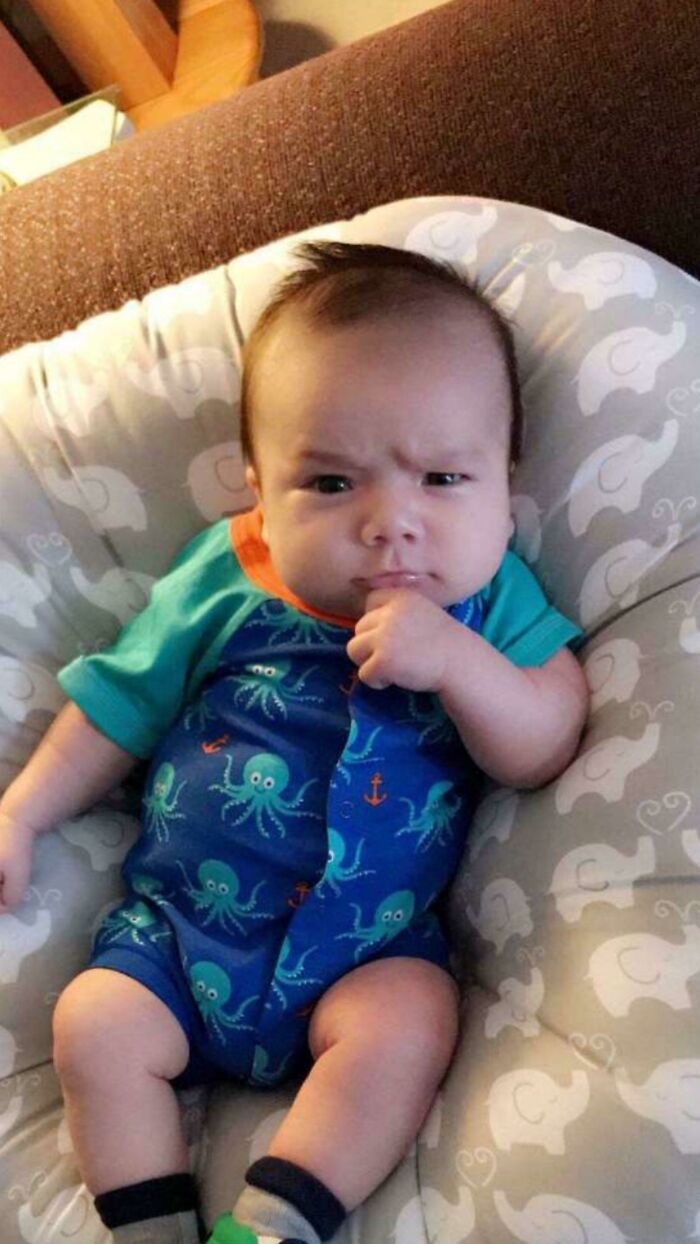 Baby wearing an octopus outfit sitting on a cushion, pulling off a hilarious and creative pose with a thoughtful expression.