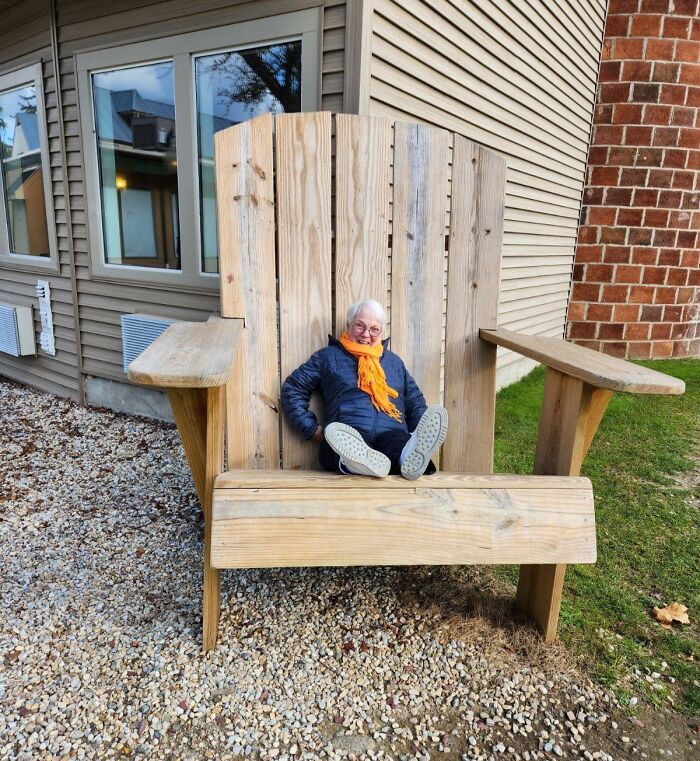 Elderly person sitting in an oversized wooden chair outdoors, a puzzling scene in unedited photos that mess with the brain.