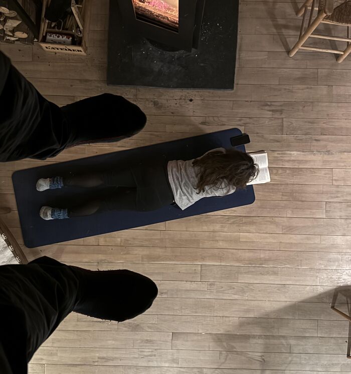 Overhead view of a person lying on a mat reading a book near a fireplace, creating a brain-teasing perspective.