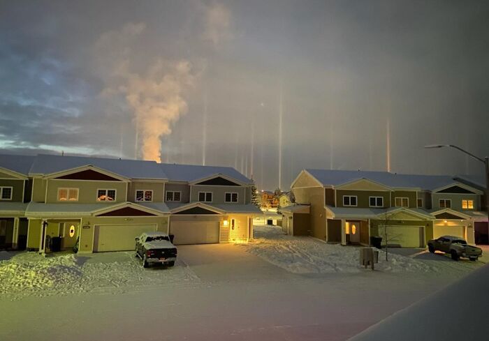 Snow-covered houses at night with light pillars in the sky, an unedited photo that might mess with your tired brain.