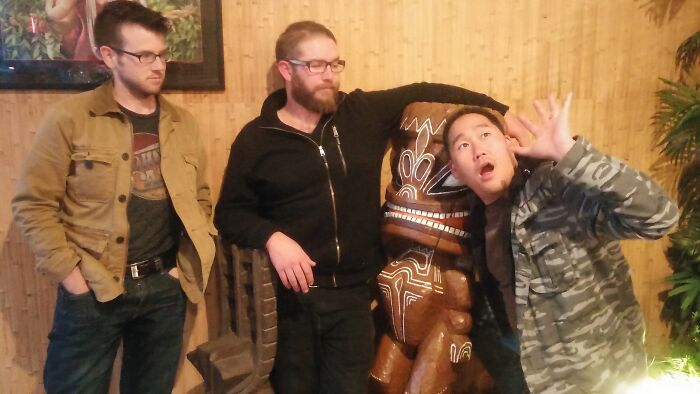 Three men posing creatively with a carved wooden statue, showcasing hilarious and creative poses pulled off perfectly.