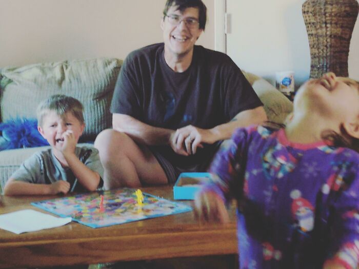 A father and two kids playing a board game at home, capturing a funny moment of sibling rivalry and childhood memories.