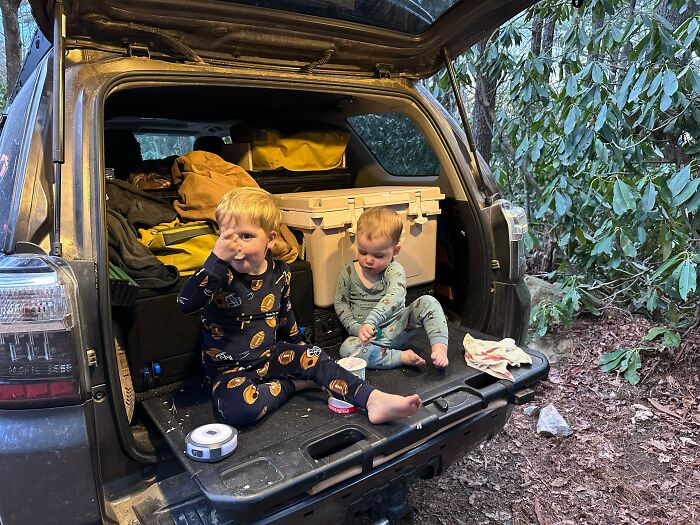 Two young boys in pajamas eating in the back of an SUV, an image of great dad life.