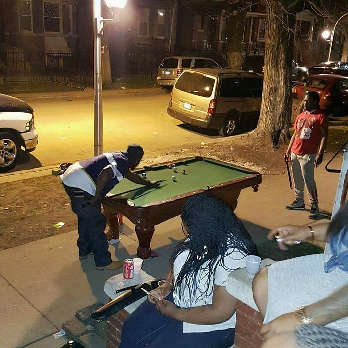 Outdoor nighttime pool game on the sidewalk with people socializing, capturing the essence of urban life in US states.