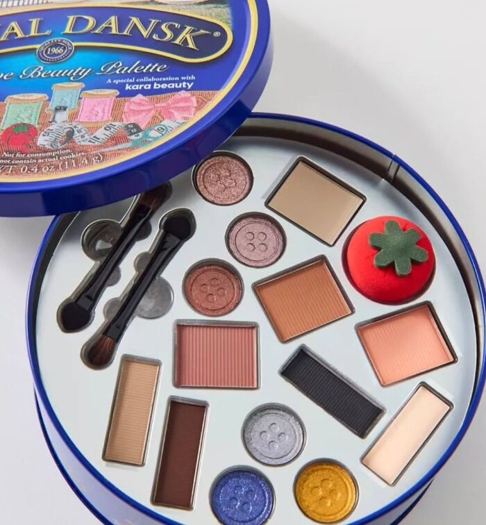 Vintage Royal Dansk cookie tin repurposed as a makeup palette with eyeshadows and a tomato-shaped brush, nostalgic millennial item.