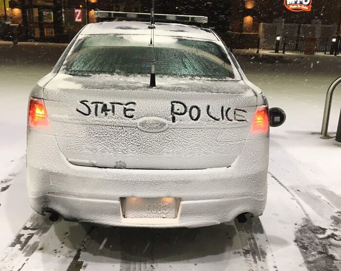 Snow-covered state police car with words written on the back window, capturing the essence of a winter scene in the US.