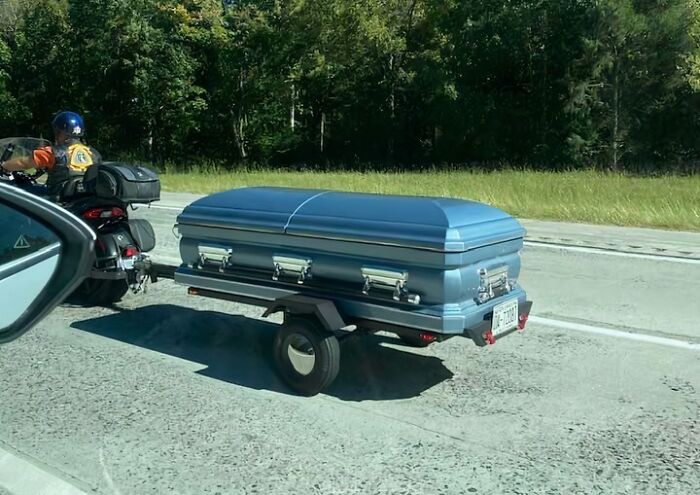 Motorcycle towing a blue coffin trailer on a rural highway, capturing unique and unusual scenes in US states.
