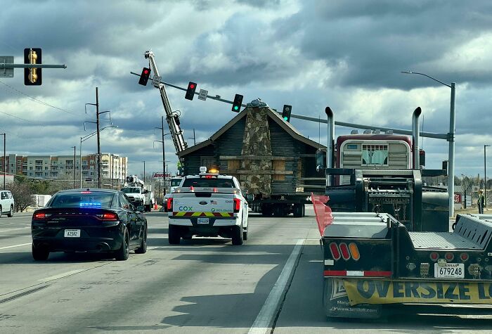Oversized house being transported on highway, escorted by police and utility vehicles, capturing essence of each US state.