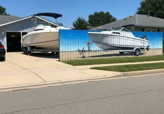 A painted fence shows a realistic boat image matching the real boat parked behind in a suburban driveway scene.