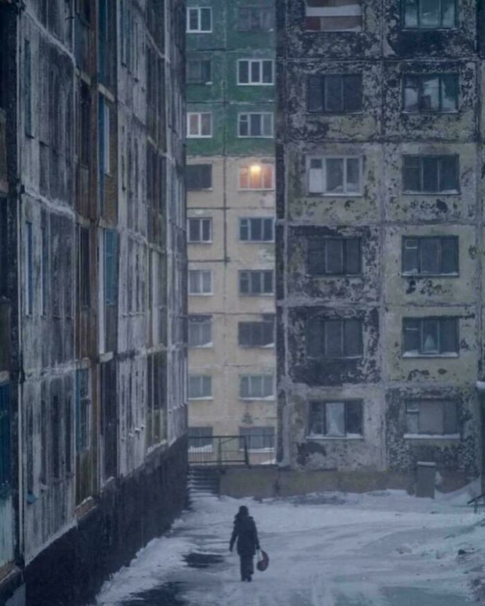 Person walking in snowy alley between dilapidated apartments in urban hell area