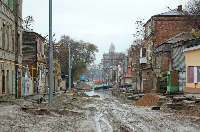 Muddy and damaged urban street with old buildings and construction in urban hell