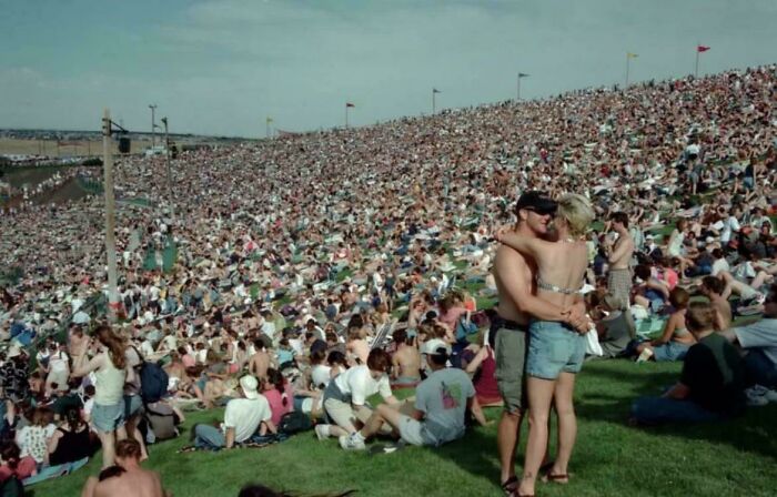 Large crowd at an outdoor event with people sitting on grass and a couple embracing in the foreground, showcasing interesting vault moments.