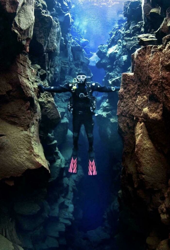 Scuba diver exploring an underwater rocky crevice, showcasing interesting vault of nature's bizarre and cool oddities.