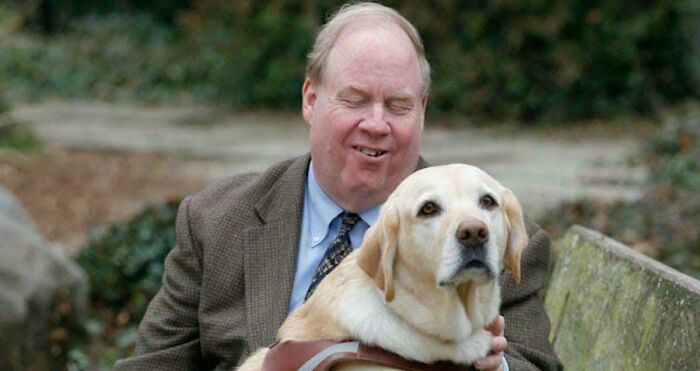 Man in a brown jacket with a guide dog on a bench, representing interesting vault stories and oddities from our world.