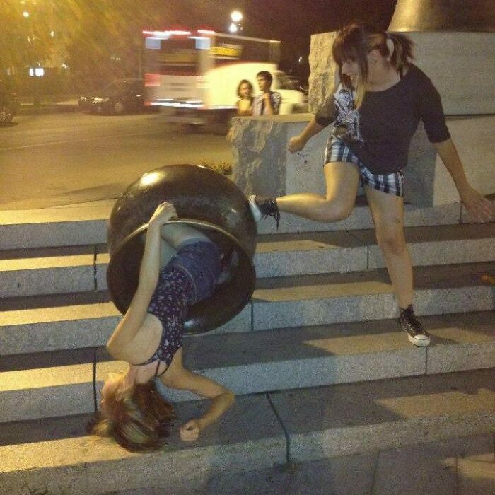 Two women pulling off creative poses on stone steps at night, one stuck inside a large black object.