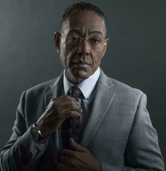 Mature man adjusting tie, wearing glasses and a gray suit, representing interesting vault of stories and oddities.