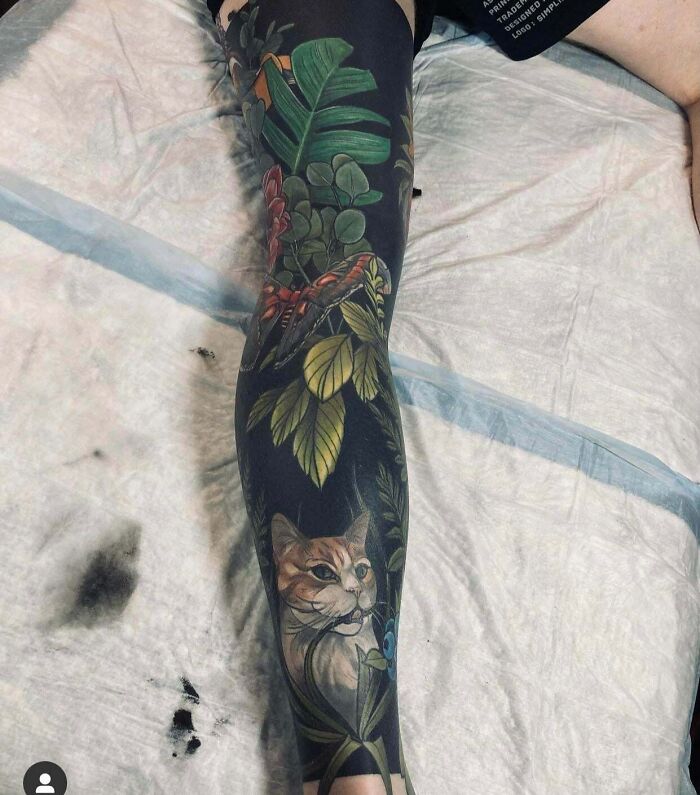 Full leg tattoo featuring a realistic cat, colorful leaves, and a butterfly in a cool tattoo design.